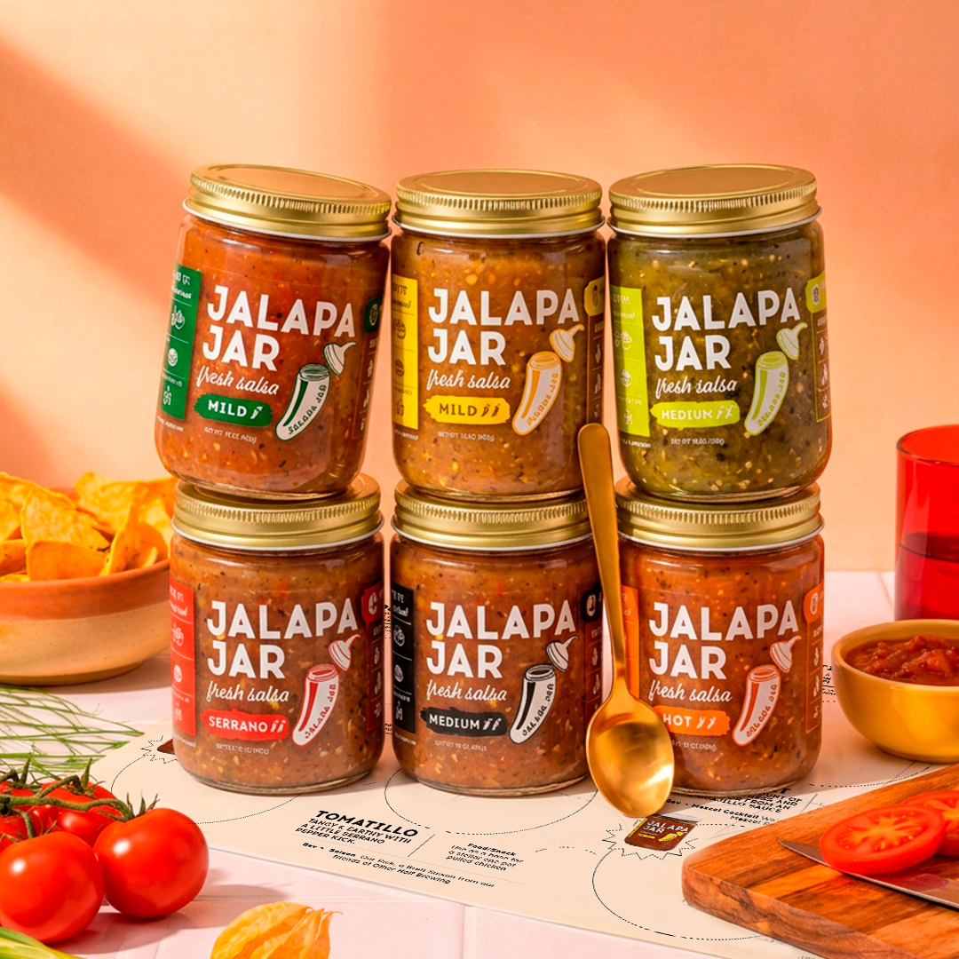 Jars of Jalapa Jar salsa on a table with ingredients and a colorful background