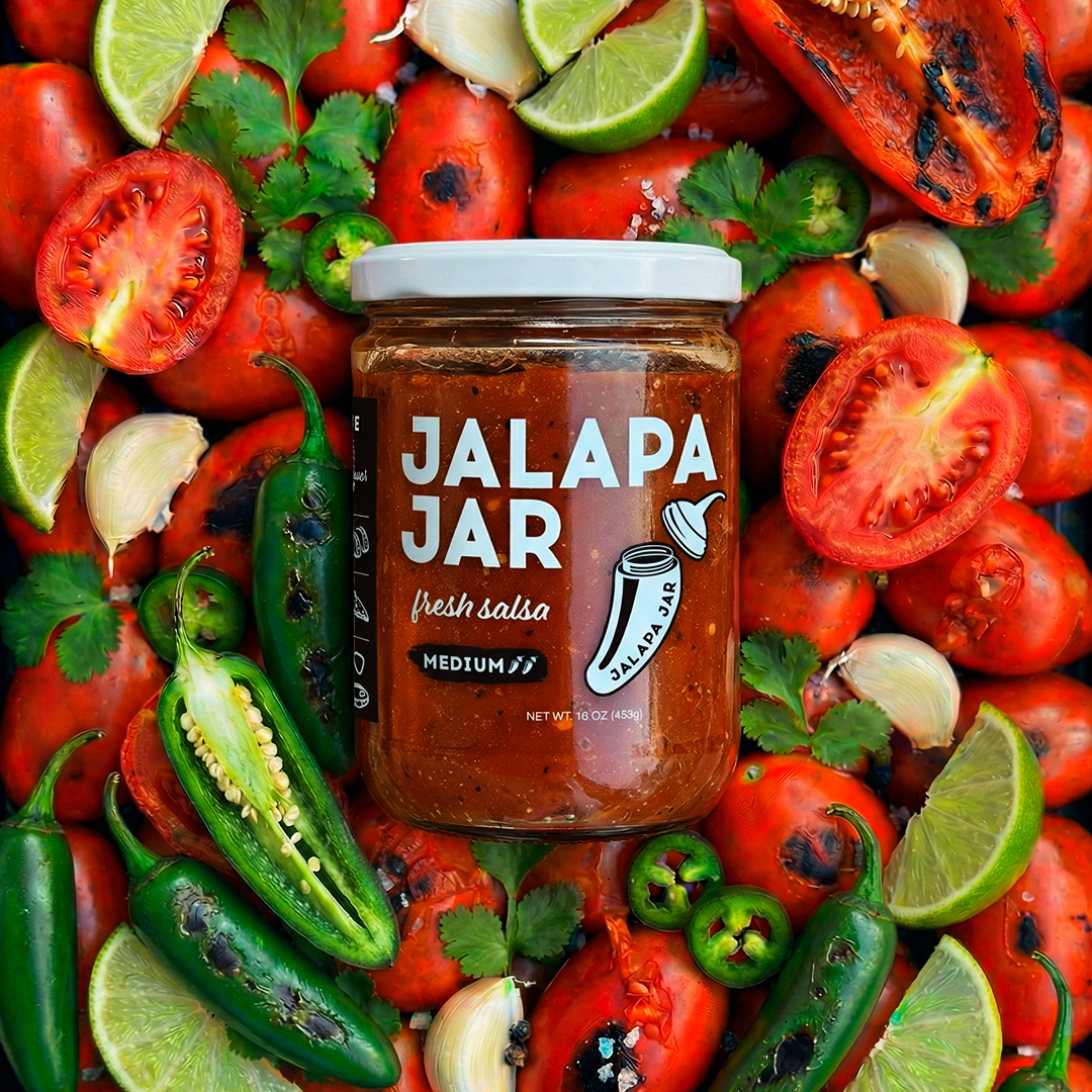 Jalapa Jar salsa surrounded by fresh ingredients like tomatoes, jalapenos, and limes.