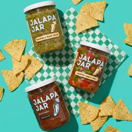Three jars of Jalapa Jar salsa on a checkered tablecloth with tortilla chips around them.